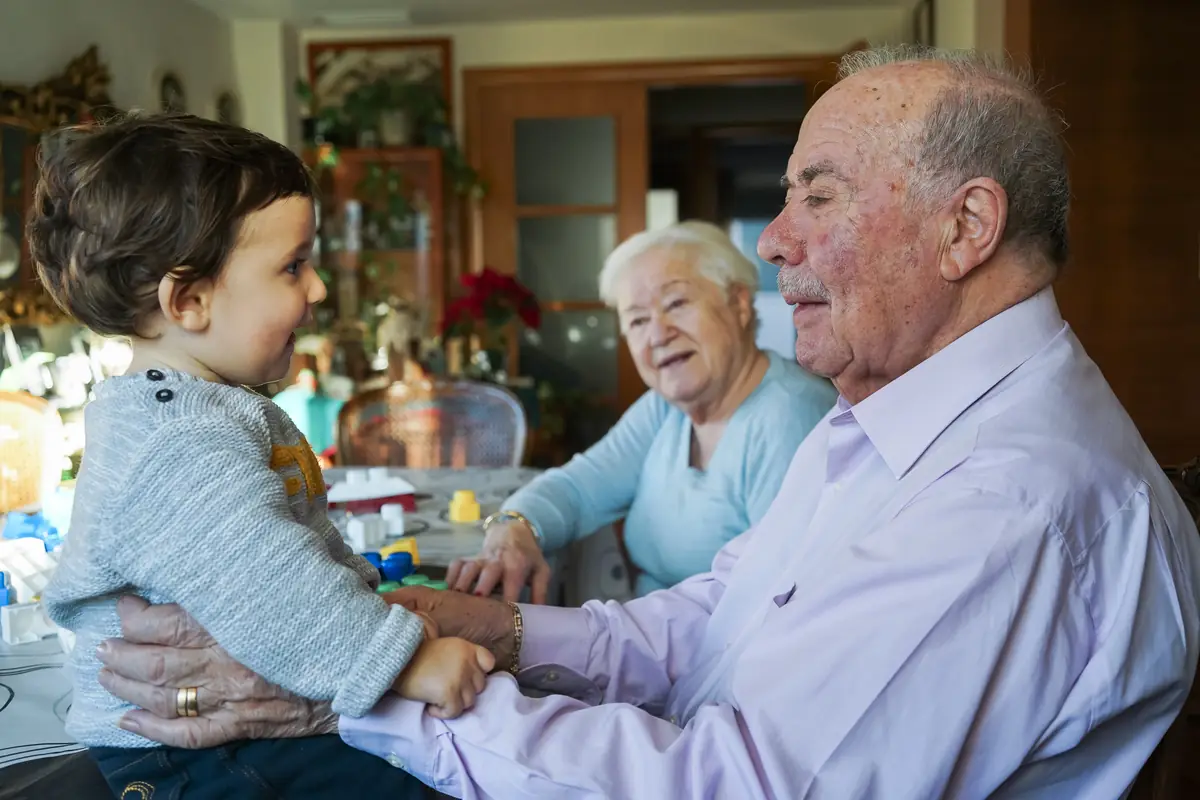Stock photograph: an older man holding a toddler with an older woman alongside at home