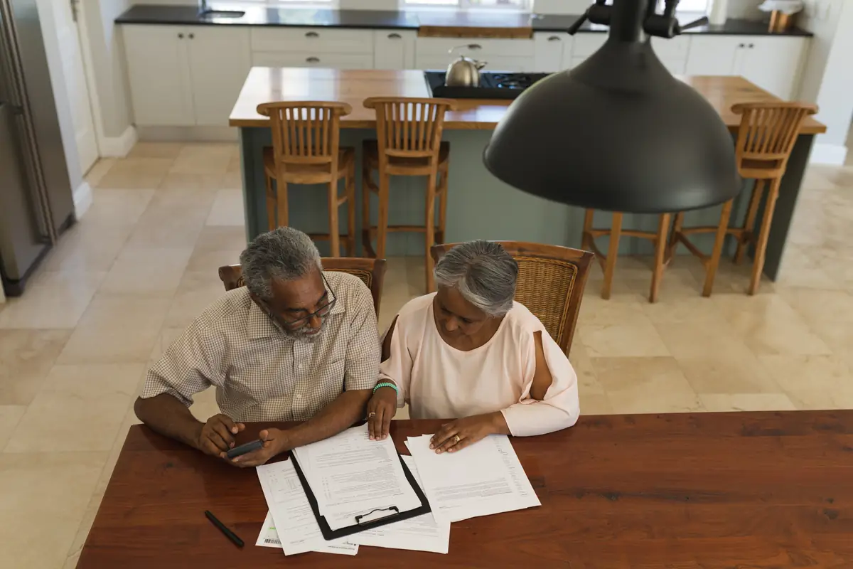 Stock photograph: an older couple reviewing paperwork and a phone at a table at home